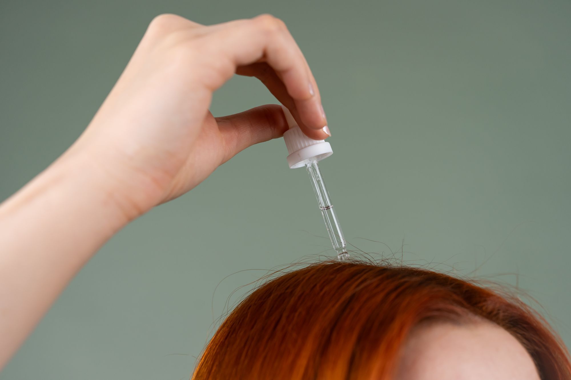 A dropper applying serum along a part in red hair