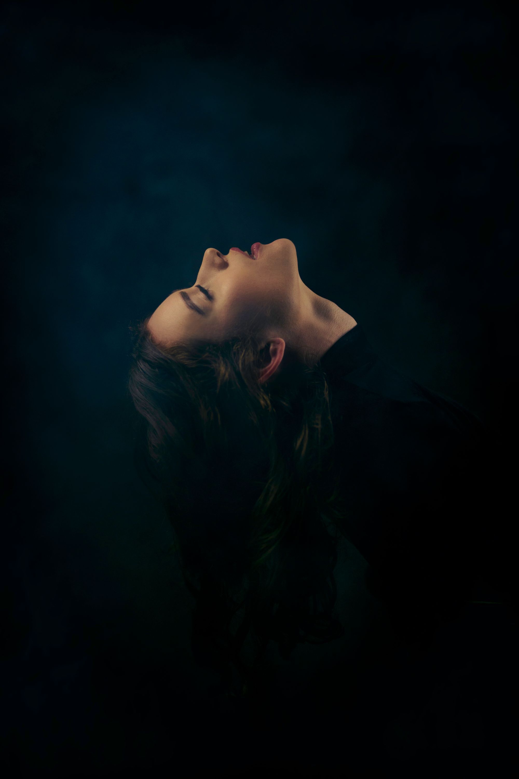 A woman in profile with her head tilted back in near darkness