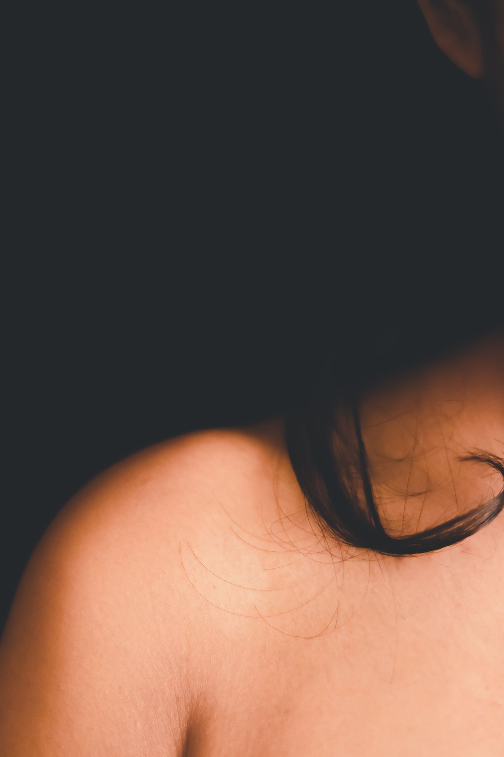 A bare shoulder and dark hair against a dark background